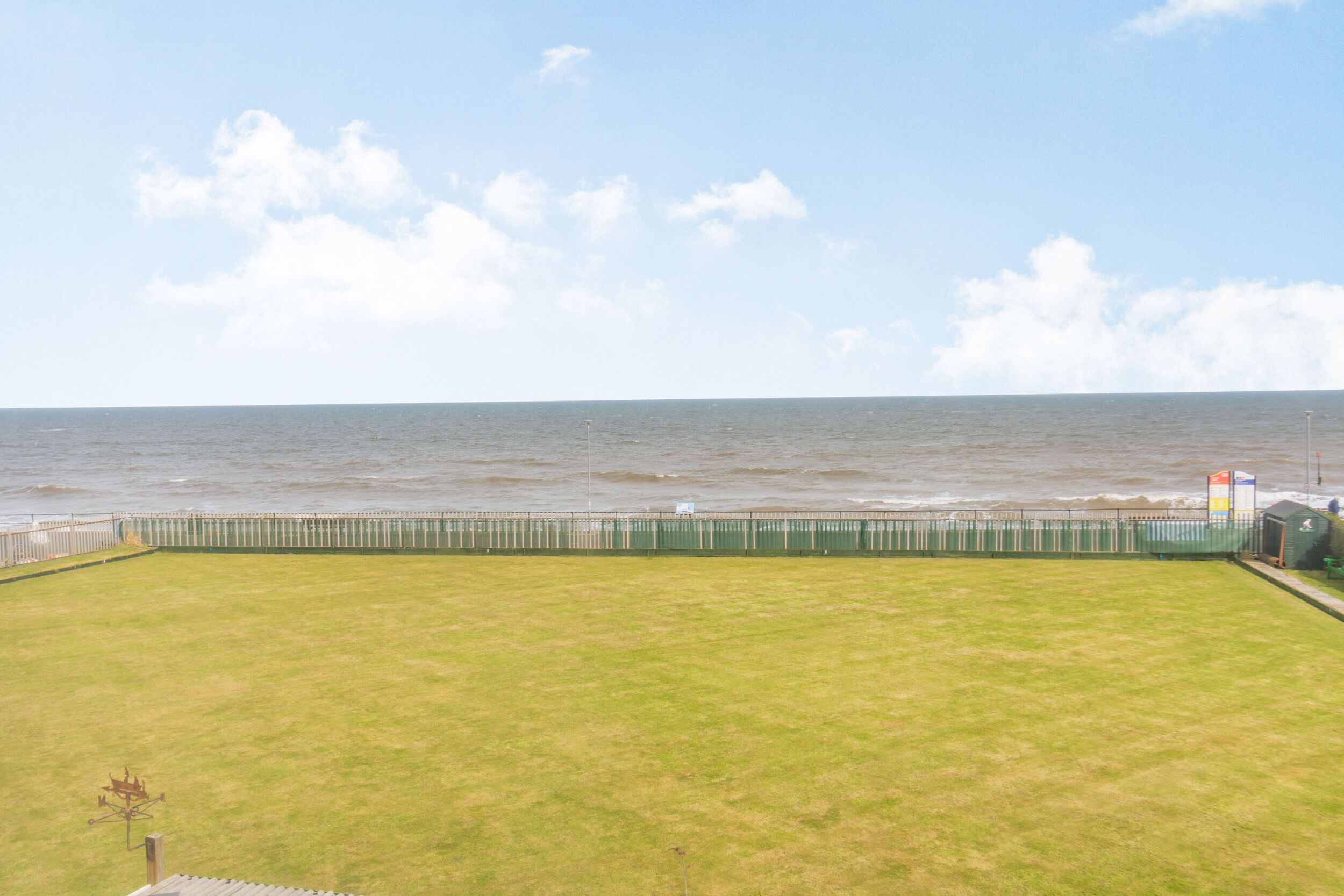 A grassy area with a view of the sea and a fence.