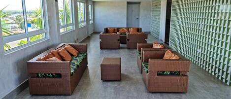 A spacious indoor area with wicker furniture and large windows offering views of greenery and buildings.