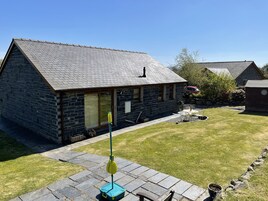 A stone house with a sloped roof, a front door, and a small patio area with a lawn and a table.