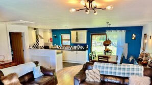A living room with two brown leather sofas, a wooden coffee table, and a kitchen in the background. - Yr Encil (Gaerwen)
