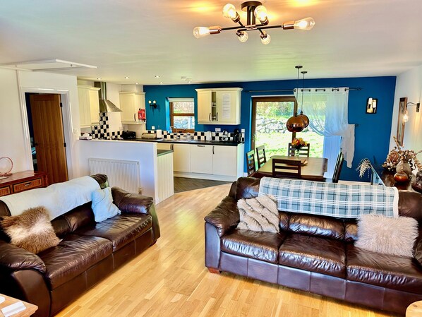 A living room with two brown leather sofas, a wooden coffee table, and a kitchen in the background.