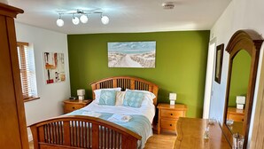A bedroom with a wooden bed, green walls, a painting, bedside lamps, and a mirror. - Yr Encil (Gaerwen)