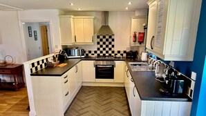 A modern kitchen with white cabinetry, a herringbone-patterned floor, and a central island. - Yr Encil (Gaerwen)