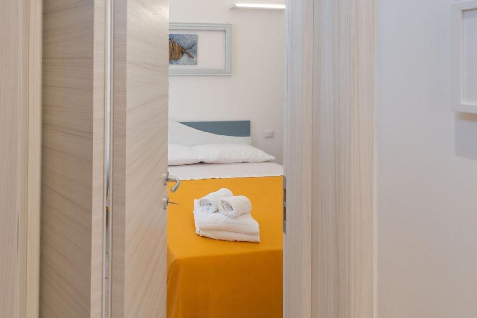 Un corridoio stretto che porta a una stanza con un letto e un tavolo giallo con asciugamani piegati.