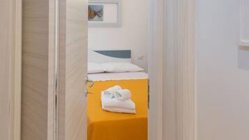 Un corridoio stretto che porta a una stanza con un letto e un tavolo giallo con asciugamani piegati.