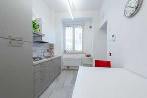 A compact kitchen with modern appliances, a window with curtains, and a red chair.