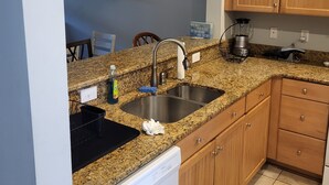 Eine Küche mit Granit Arbeitsplatten, Holzschränken, einem Geschirrspüler und einem schwarzen Mülleimer.
