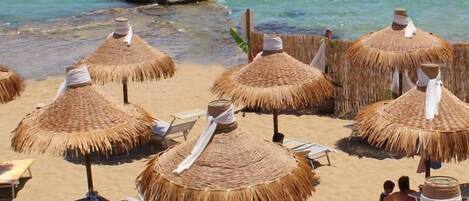 A beach with thatched umbrellas and lounge chairs.