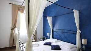 A bedroom with a four-poster bed, white linens, and a blue accent wall. - Hotel Noto Marina a Mare Spa (Noto)