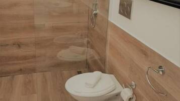 A modern bathroom with a glass shower enclosure, a toilet, a bidet, and a sink.