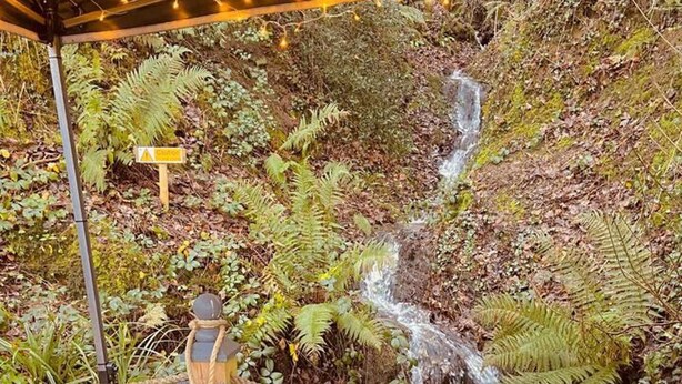 Ein Sitzbereich im Freien mit Tisch und Kissen, einer Hängesitzschaukel und einem Wasserfall im Hintergrund.