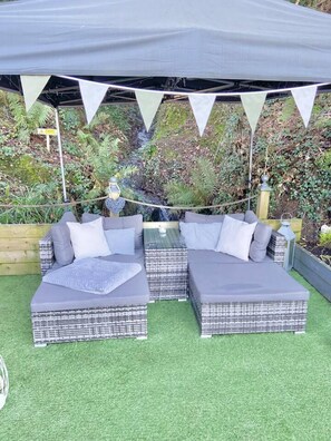 A sectional sofa with a grey cushion and white pillows, set on artificial grass under a grey canopy. - A Beautiful, Unique Lodge, Made for two (Lampeter)