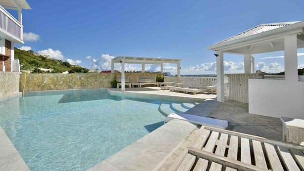 Ein klares Schwimmbecken mit Liegestühlen und einer Pergola, umgeben von Steinmauern und Blick auf das Meer.