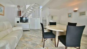 Ein modernes Wohnzimmer mit einem weißen Sofa, einem Esstisch mit Stühlen, einem Fernseher und einer Treppe.