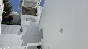 Ein schmaler, weiß getünchter Korridor mit Stufen, die zu einer Holztür und einem Balkon führen.