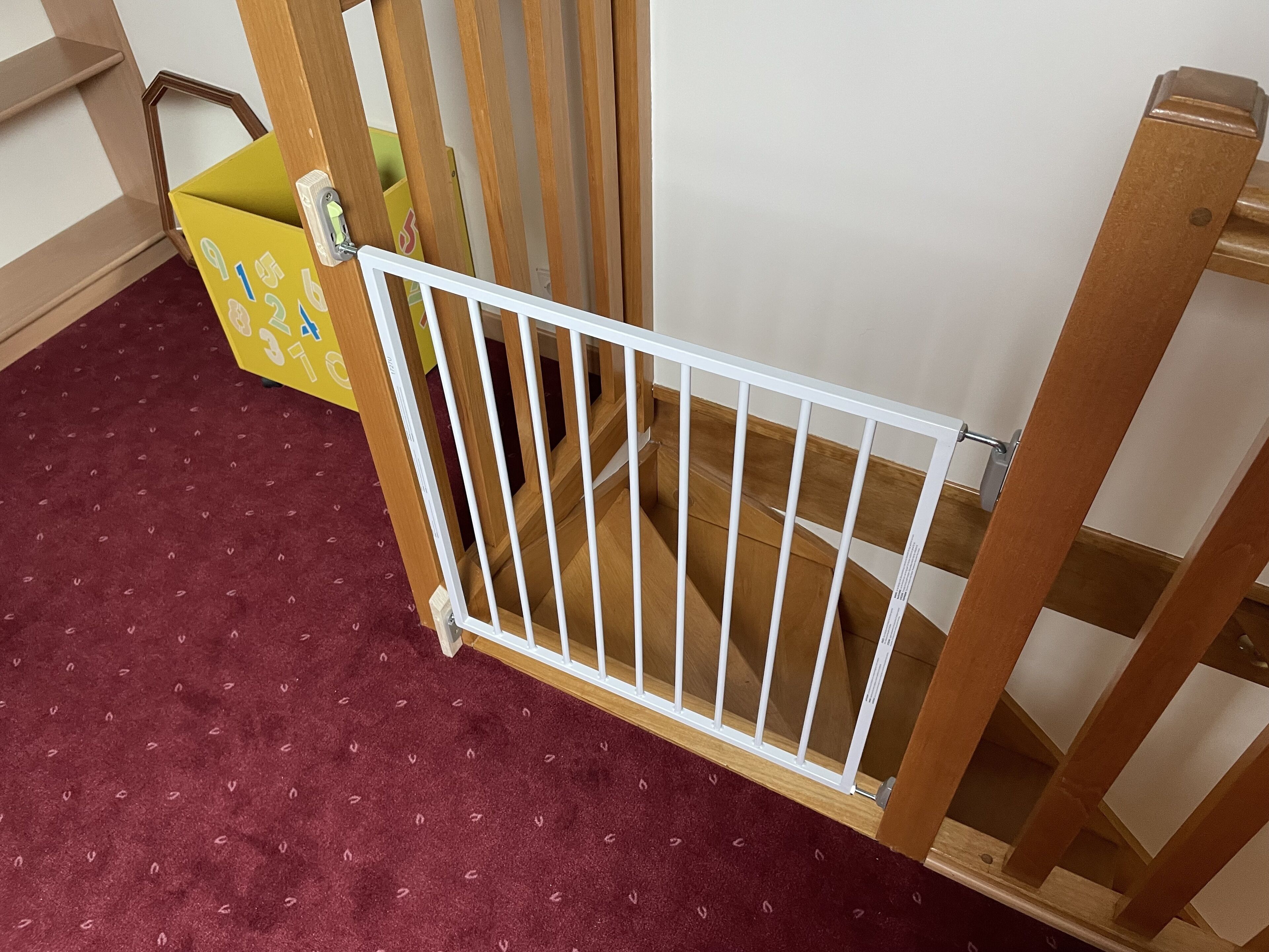 A wooden crib with a white safety gate in a room with a red carpet.