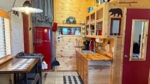 A compact kitchen with wooden cabinets, a red refrigerator, a dining table with chairs, and a red leather couch. - Bear Haven on Northwoods Road (Greer)