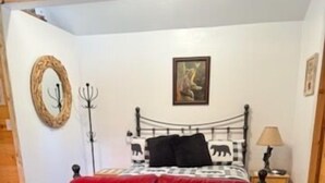 A bedroom with a red leather sofa, a bed with a checkered blanket, a painting on the wall, and a wooden floor. - Bear Haven on Northwoods Road (Greer)