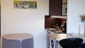 A compact kitchen with a washing machine, a coffee maker, and a dining area with a round table and two chairs. - Studio Mas du Tanit (Antibes)