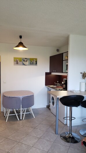 A compact kitchen with a washing machine, a coffee maker, and a dining area with a round table and two chairs.