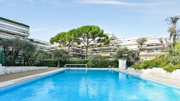 A swimming pool with a tree in the center, surrounded by a multi-story building with balconies. - Studio Mas du Tanit (Antibes)
