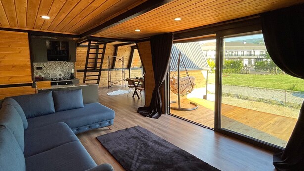 Een modern interieur met een houten plafond, een hoekbank, een zwart tapijt en uitzicht op de omgeving door grote ramen.