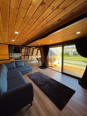 Un interior moderno con techo de madera, un sofá modular, un tapete negro y vistas al exterior a través de amplios ventanales.