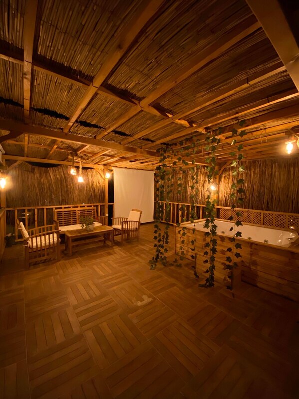 Una habitación con piso y techo de madera, una bañera blanca y un banco de madera.