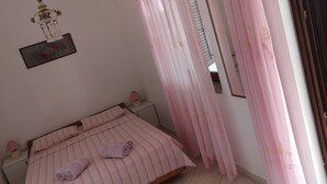 Un dormitorio con cama, dos lámparas de noche, un cuadro enmarcado en la pared y cortinas rosas.