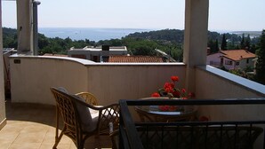 Un balcón con vista al mar, una mesa con sillas y un jarrón de flores.