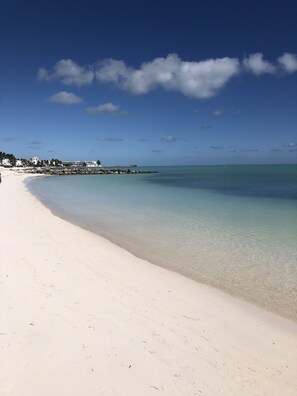 A beach with clear turquoise water, white sand, and a few buildings in the background. - 1st Floor, Private Sandy Beach, Heated Pool, Perfect Sunsets on Key Colony Beach (Key Colony Beach)