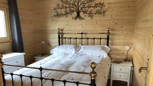 Quarto com painéis de madeira, uma cama, mesas de cabeceira, uma luminária e um painel decorativo em formato de árvore.