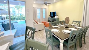 A dining area with a table set for four, a television on a cabinet, and a view of the pool outside. - 5br/5ba/5mi Disney • Heated Pool/SPA • Free Uber rides to parks! (Kissimmee)