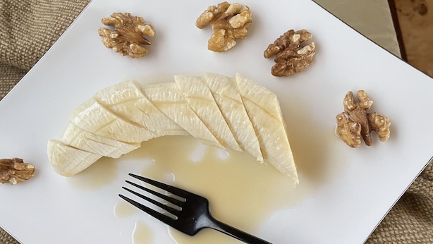 Ein weißer Teller mit Bananenscheiben, Walnüssen und einer Gabel auf einer strukturierten, beige farbenen Oberfläche.