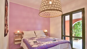 Un dormitorio con cama, lámparas de noche, un cabecero decorativo y un ventanal con vistas a zonas verdes.