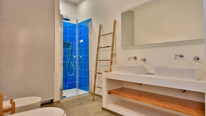 Un baño moderno con cabina de ducha de vidrio, una escalera de madera, un lavamanos blanco y un inodoro.