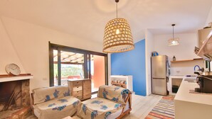 Una sala de estar acogedora con un sofá, una mesa de centro y una chimenea. Hay una zona de cocina con un refrigerador y un lavamanos.