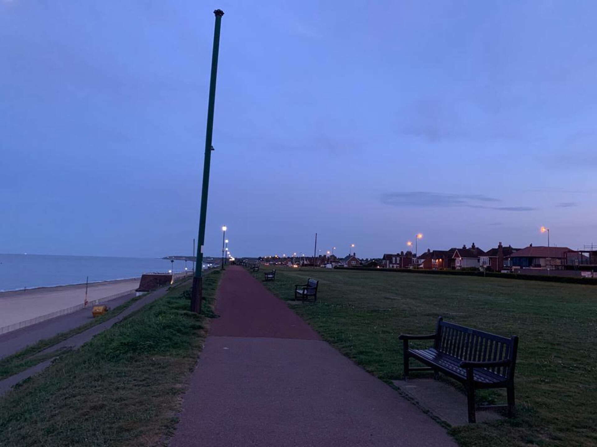 A coastal walkway with benches, a path, and street lamps.