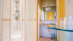 A bathroom with a glass shower enclosure, a sink with a marble countertop, and a mirror above the sink.