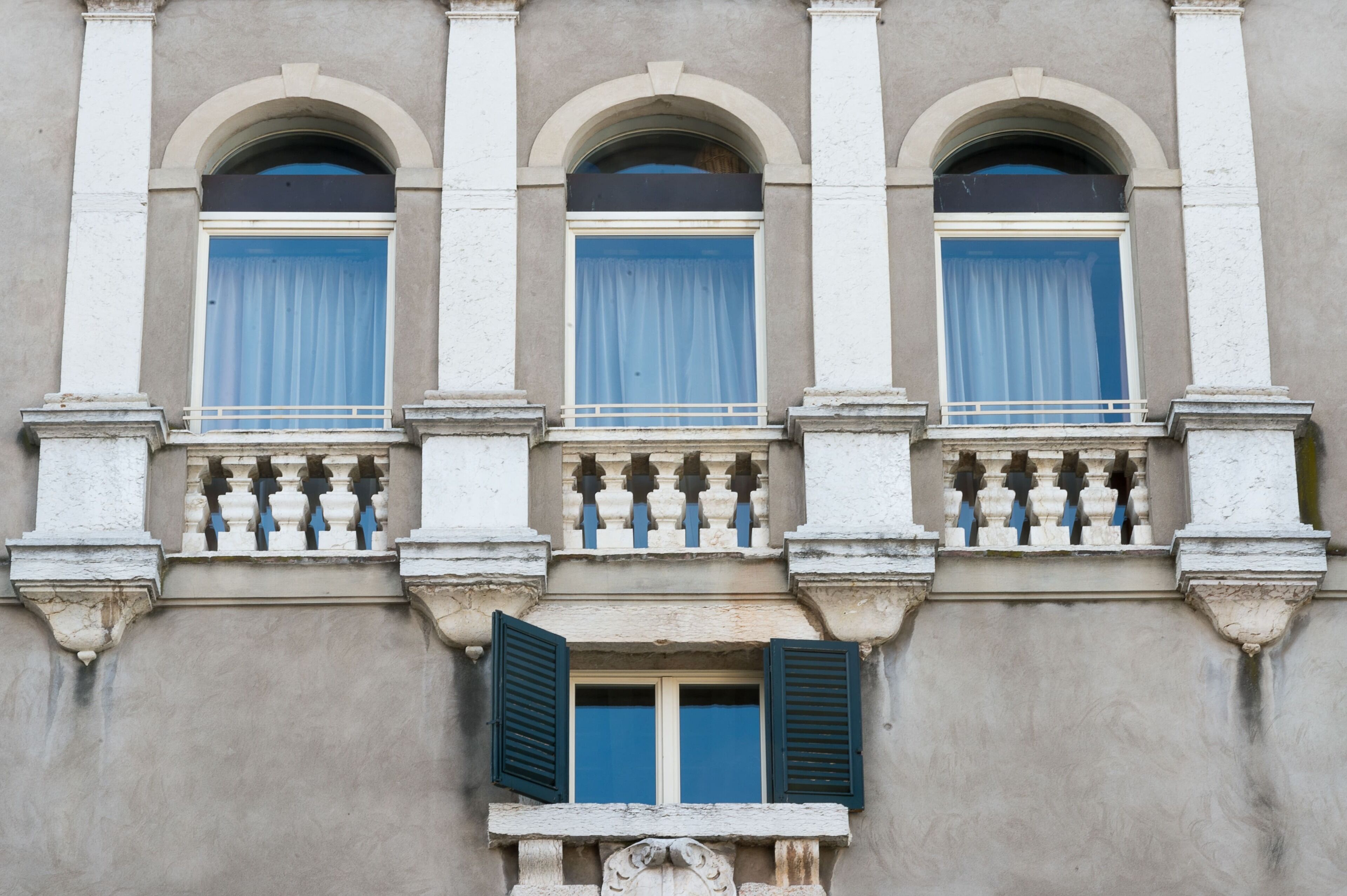 A building facade with three arched windows, each with a blue curtain, and a balcony with white balustrades.