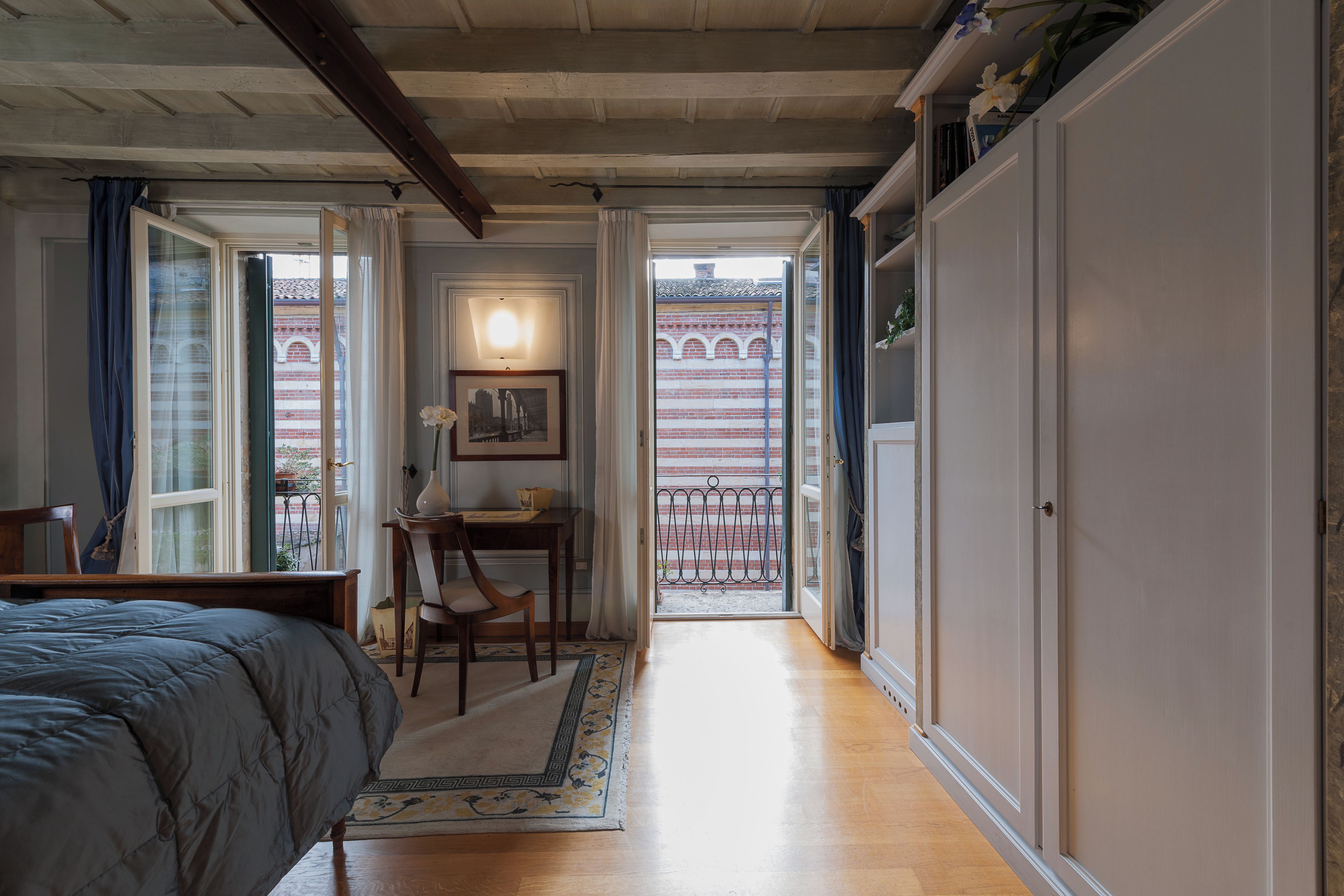 Ein Schlafzimmer mit Bett, Schreibtisch und Blick auf einen Balkon mit Geländer.