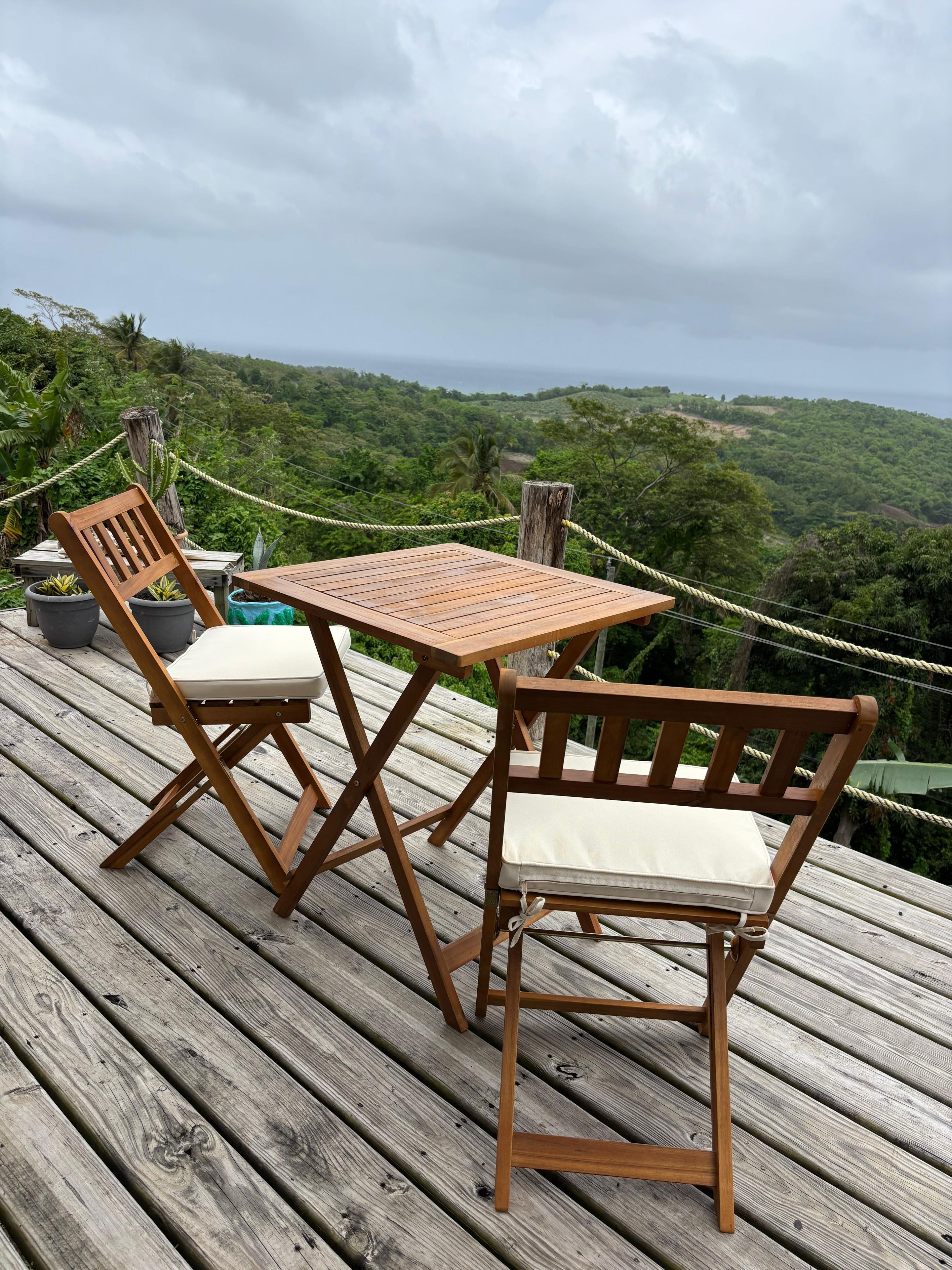 A wooden deck with a table and two chairs, overlooking a lush green landscape.
