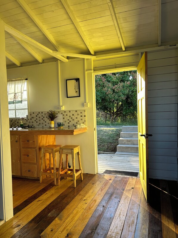A kitchen with wooden cabinets, a countertop, stools, and a view of the outdoors.