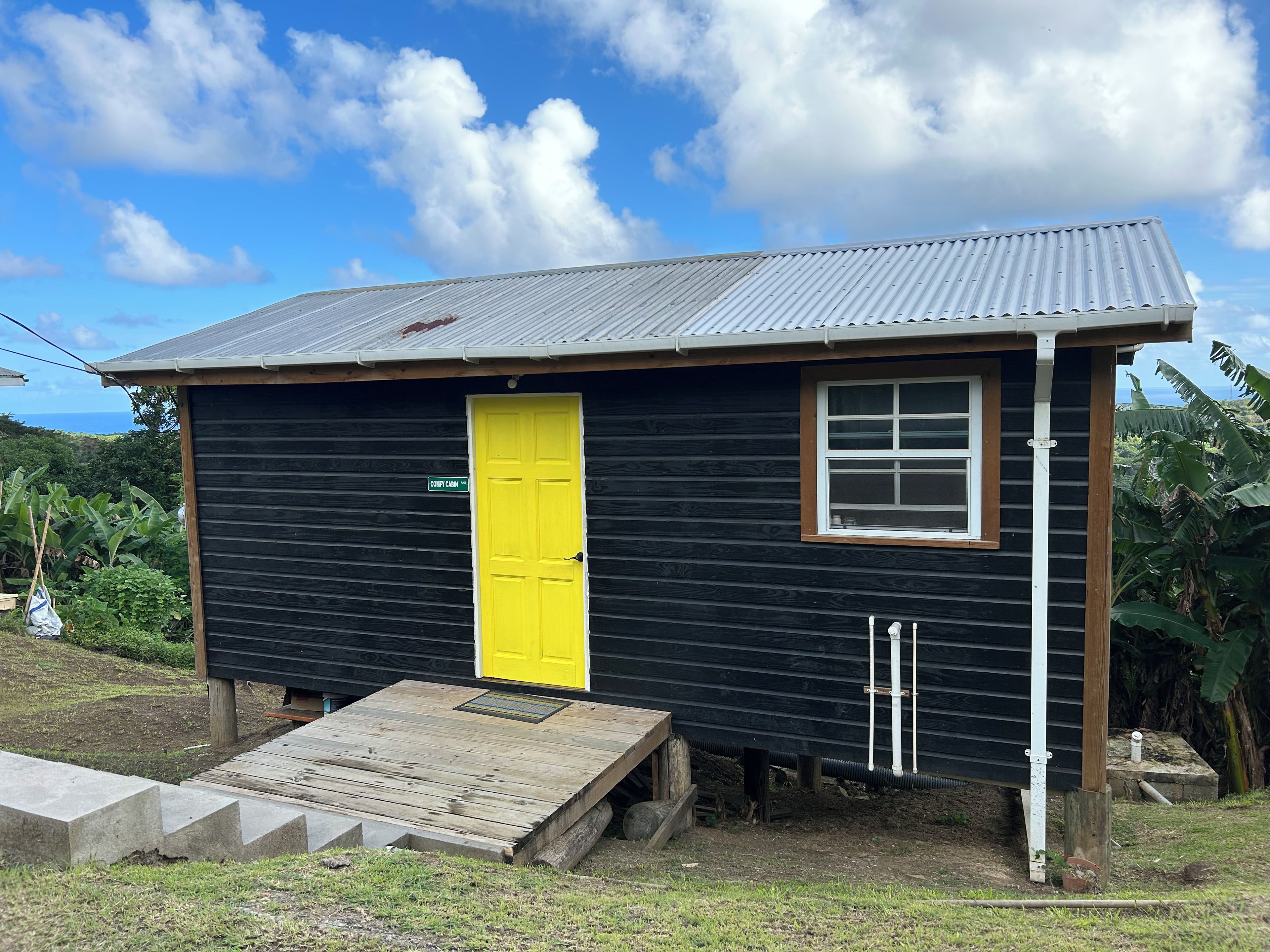 A small wooden cabin with a yellow door, a window, and a ramp leading to the entrance.