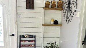 Een gezellige hoek met een houten stoel, een klein krukje, een plant in pot en planken met decoratieve voorwerpen.