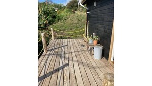 Een houten terras met een touwbordes, planten in potten en een gebouw op de achtergrond.