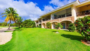 A two-story building with a balcony, a well-maintained lawn, and palm trees. - Punta Cana Condo with Swimming Pool in Cocotal (Punta Cana)