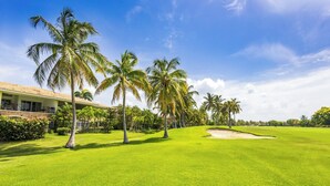 A golf course with a building on the left, palm trees, and a clear sky. - Punta Cana Condo with Swimming Pool in Cocotal (Punta Cana)