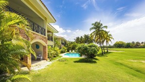 A two-story building with a swimming pool, surrounded by a well-maintained lawn and palm trees. - Punta Cana Condo with Swimming Pool in Cocotal (Punta Cana)