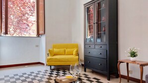 Ein Zimmer mit einem gelben Sofa, einem schwarzen Schrank, einem kleinen Tisch mit einer Vase und einem karierten Boden.